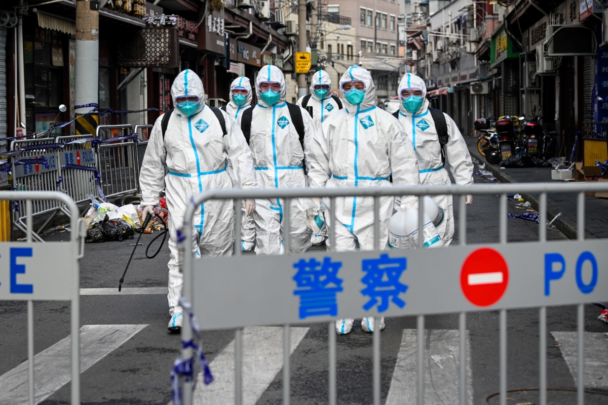 People wearing protective coveralls and masks behind a street barrier.